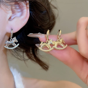Detail of rocking horse stud earrings with hammer texture and pearl accents in gold and silver