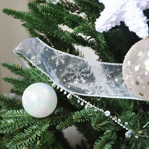 Sparkling white snowflake and dot ribbons with ornaments on a green Christmas tree