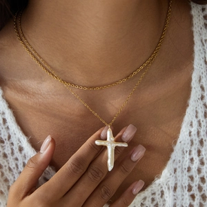 Detail of layered gold chain necklace featuring a white baroque pearl cross pendant