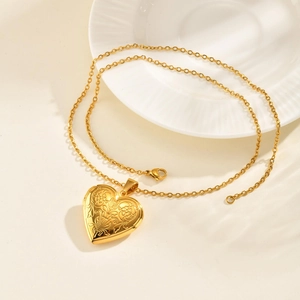 Detail of golden heart locket necklace with vintage floral engraving on white ceramic tray