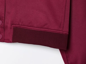 Detailed macro view of burgundy jacket showing ribbed cuff and precise double stitching