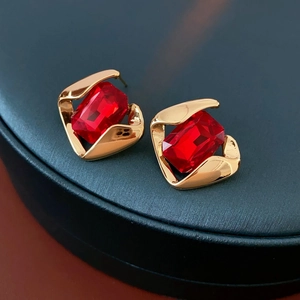 Close-up of geometric gold earrings featuring large rectangular red crystal gemstones