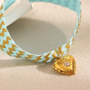 Macro detail of a light blue woven ribbon bracelet with a gold heart locket pendant