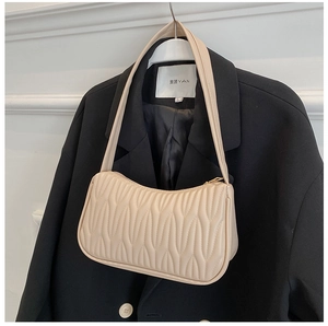 Detailed view of beige pleated shoulder bag on a black blazer showing vertical textures