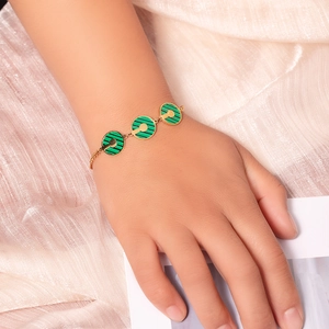 Dettaglio di un bracciale dorato con tre ciondoli in malachite verde su seta rosa
