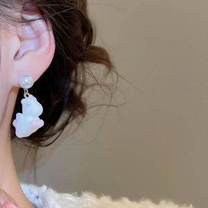 Detailed close-up of a pearl stud earring with a cute white puppy pendant on a model's ear