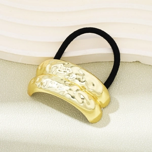 Detailed close-up of golden hammered metal hair tie with durable black elastic band