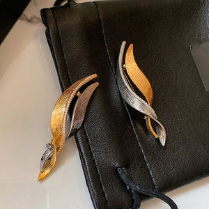 Detailed view of twisted zircon brooches with brushed metal texture on a leather pouch