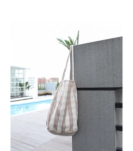 Close-up of beige and white striped canvas tote bag hanging on a stone wall by a pool