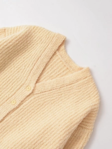 Détail d'un cardigan en grosse maille crème avec col en V et petits boutons jaunes