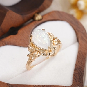 Macro detail of leaf textured gold ring with pear shaped opal on white velvet insert