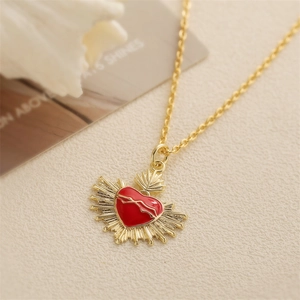 Red enamel heart pendant necklace with gold sunburst rays on textured paper background
