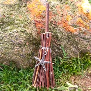 Detail of a handmade mini witch broom charm with starfish metal pendant on wood
