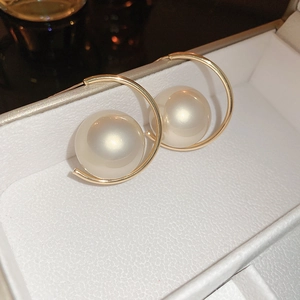 Close-up of gold C-shaped earrings with large faux pearls in a white jewelry box