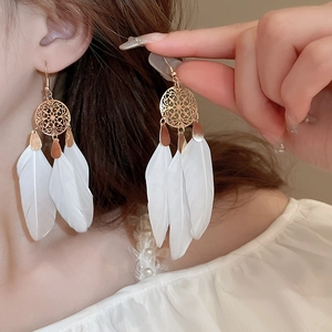 Detail of bohemian drop earrings with gold hollow discs and soft white natural feathers