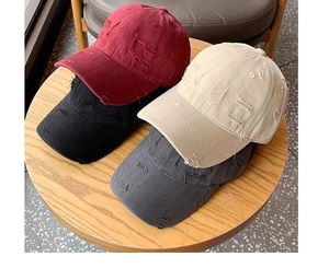 Distressed baseball caps in burgundy, black, beige, and grey on a wooden table surface