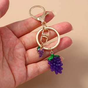 Handheld creative purple grape keychain pendant with golden metal ring on beige background