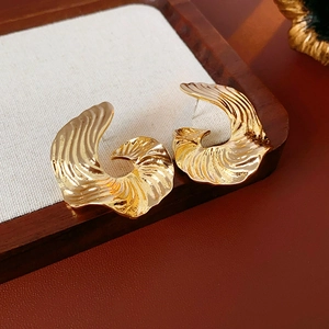 Detailed view of gold earrings with wavy shell texture on a wood display tray