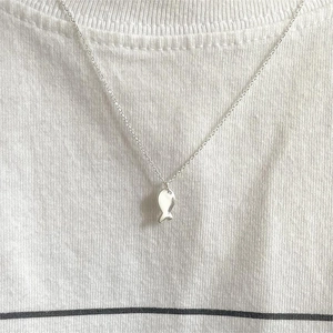 Close-up of minimalist sterling silver fish pendant necklace worn on a white t-shirt