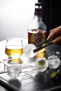 Macro detail of spherical ice mold with stainless steel tongs and clear ice balls