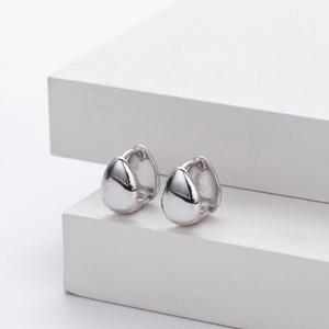 Detailed view of polished S925 sterling silver teardrop earrings on white geometric stands