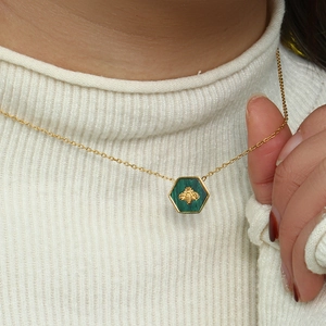 Detail of a gold hexagon pendant necklace with green malachite and a gold bee relief