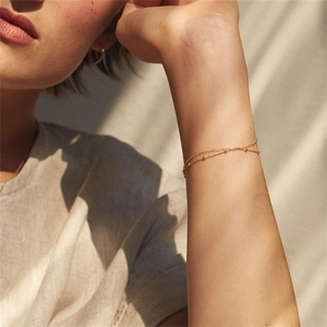 Close-up of double-layer gold chain bracelet with beads on female wrist in soft sunlight