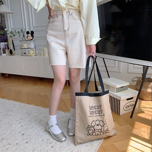 Detail view of canvas tote bag with Lucky lettering and raw edge denim shorts styling