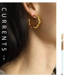 Detailed close-up of golden twisted C-shaped hoop earrings on model with metallic shine