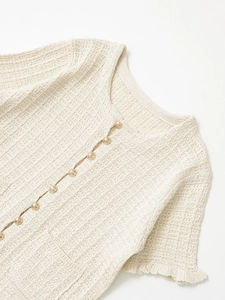 Close-up of cream knit cardigan featuring textured fabric and gold embossed buttons