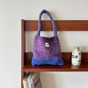 Detail of gradient purple and blue knit tote bag with visible woven texture on a wooden shelf