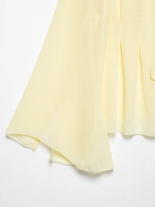 Detail of light yellow chiffon shirt featuring sheer fabric and fine edge stitching