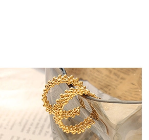 Macro shot of gold C-shaped hoop earrings with woven texture on vintage paper