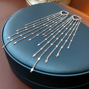 Close-up of silver metal sequin tassel earrings with hanging chains on a green jewelry box