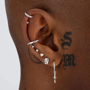 Detail of silver S925 earrings set with dagger, skull, and heart studs worn by a model