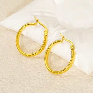 Close-up of gold hoop earrings with twisted rope texture on a white stone background