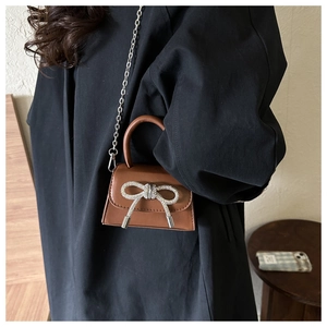 Detailed close-up of brown mini handbag with rhinestone bow and silver chain strap