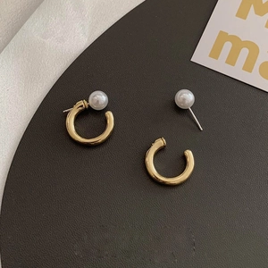 Detail of C-shaped gold pearl earrings on a textured dark plate with minimalist style