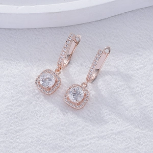 Macro detail of rose gold square drop earrings with halo crystals on white fabric