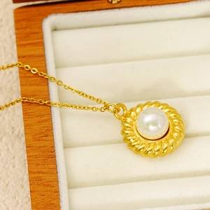 Vue macro d'un collier en acier titane doré avec pendentif perle blanche dans un coffret