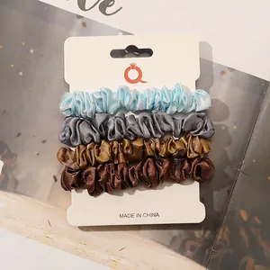 Detailed view of four satin silk scrunchies in blue, grey, gold and brown set