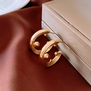 Detailed view of layered gold C-shaped earrings with metallic bead accents on silk