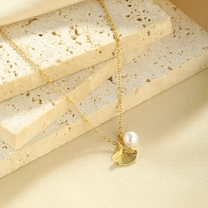 Detail of gold ginkgo leaf pendant with round white pearl on a natural stone base