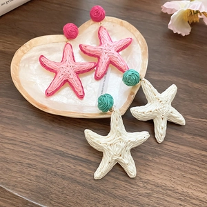 Detail of woven raffia starfish earrings in pink and white with colorful stud accents