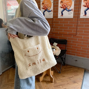 Detailansicht der flauschigen Lammwolltasche mit lächelnder Stickerei auf cremeweißem Stoff