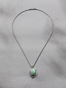 Detail of silver twisted chain with green oval gemstone pendant and crystal border
