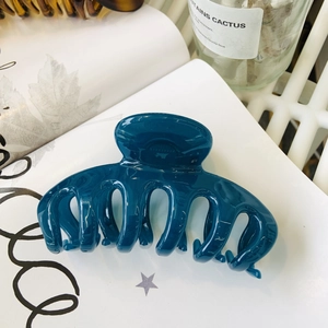 Detail of a large glossy dark blue flower hair claw clip on a minimalist white backdrop