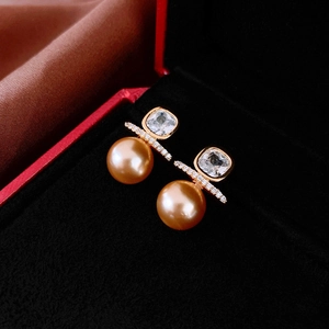 Detailed close-up of luxury square zircon and pearl gold stud earrings in red jewelry box