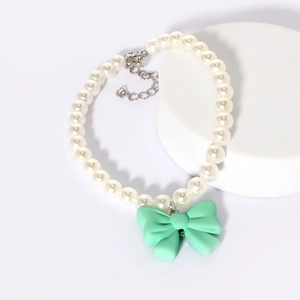 Detail of white pearl dog collar with a mint green bow pendant on a white platform