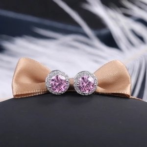 Close-up of round pink zircon halo stud earrings on elegant silk and feather background